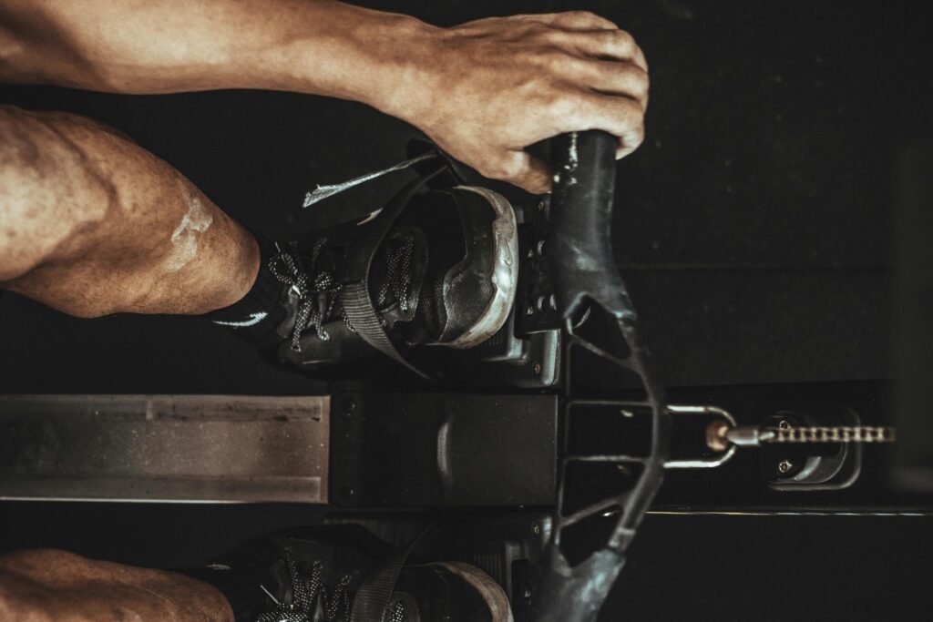 A close-up shot of a man using a rowing machine indoors, focusing on footwear and equipment.